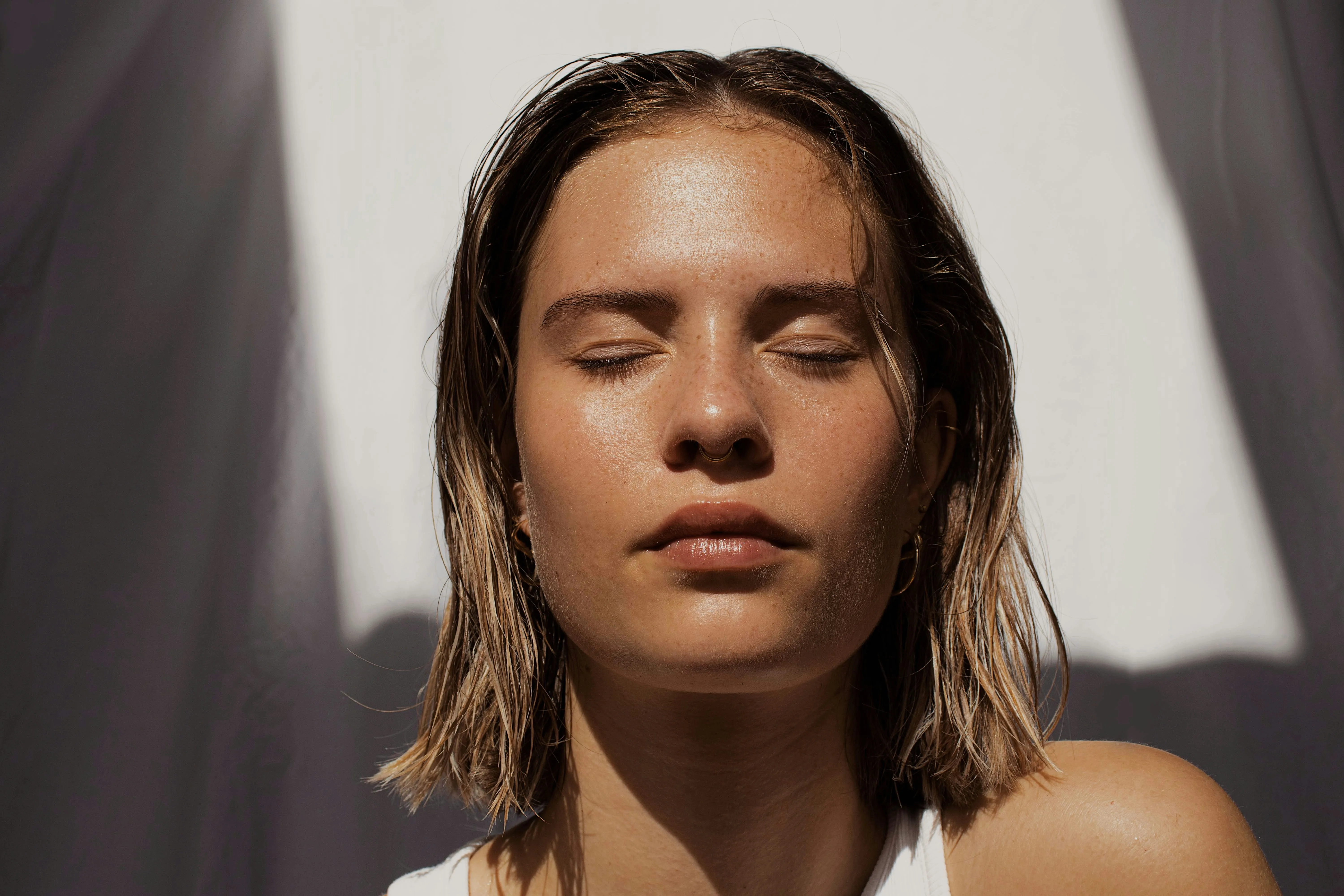 A face in warm, raked daylight, eyes closed, skin luminous.